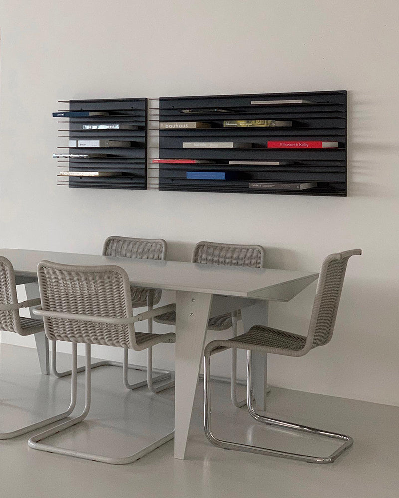 Modern Spectrum Paperback shelving system displaying books on a stylish wall above a sleek dining table and chairs.