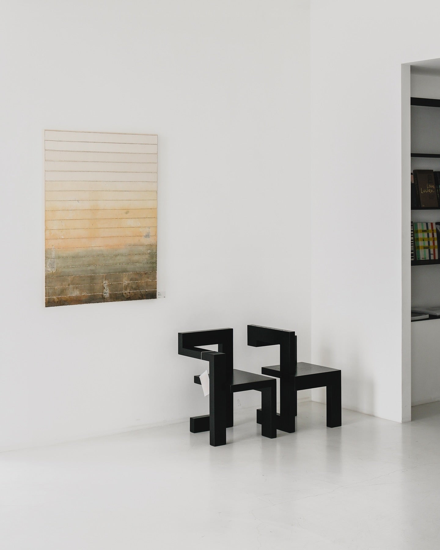 Two modern black Steltman chairs by Gerrit Rietveld in a minimalist room with an abstract painting on the wall.