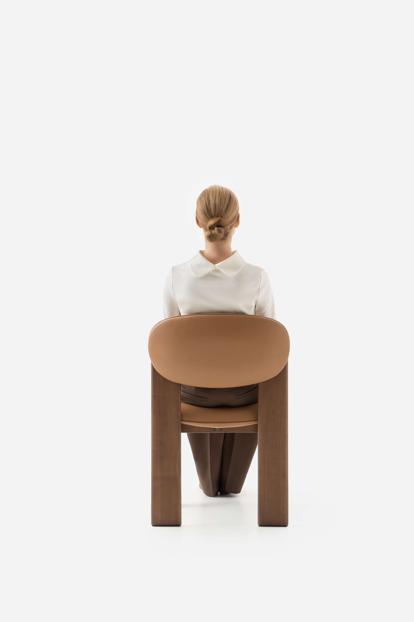 Minimalist Archipen chair by Noom with a person seated, showcasing flat twisted legs inspired by Ukrainian avant-garde design.