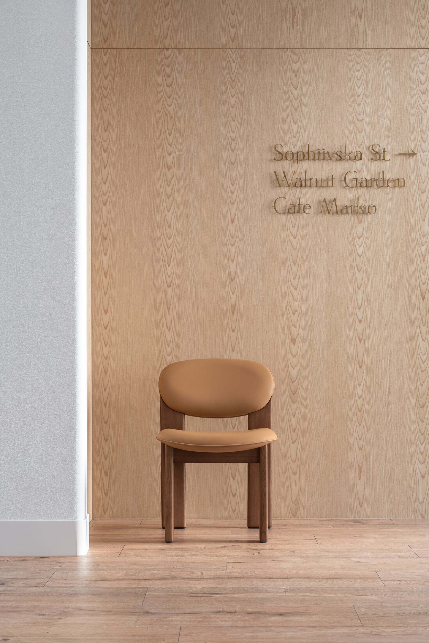 Minimalist brown chair with clean lines in front of a light wood-paneled wall with engraved text, showcasing modern home design.