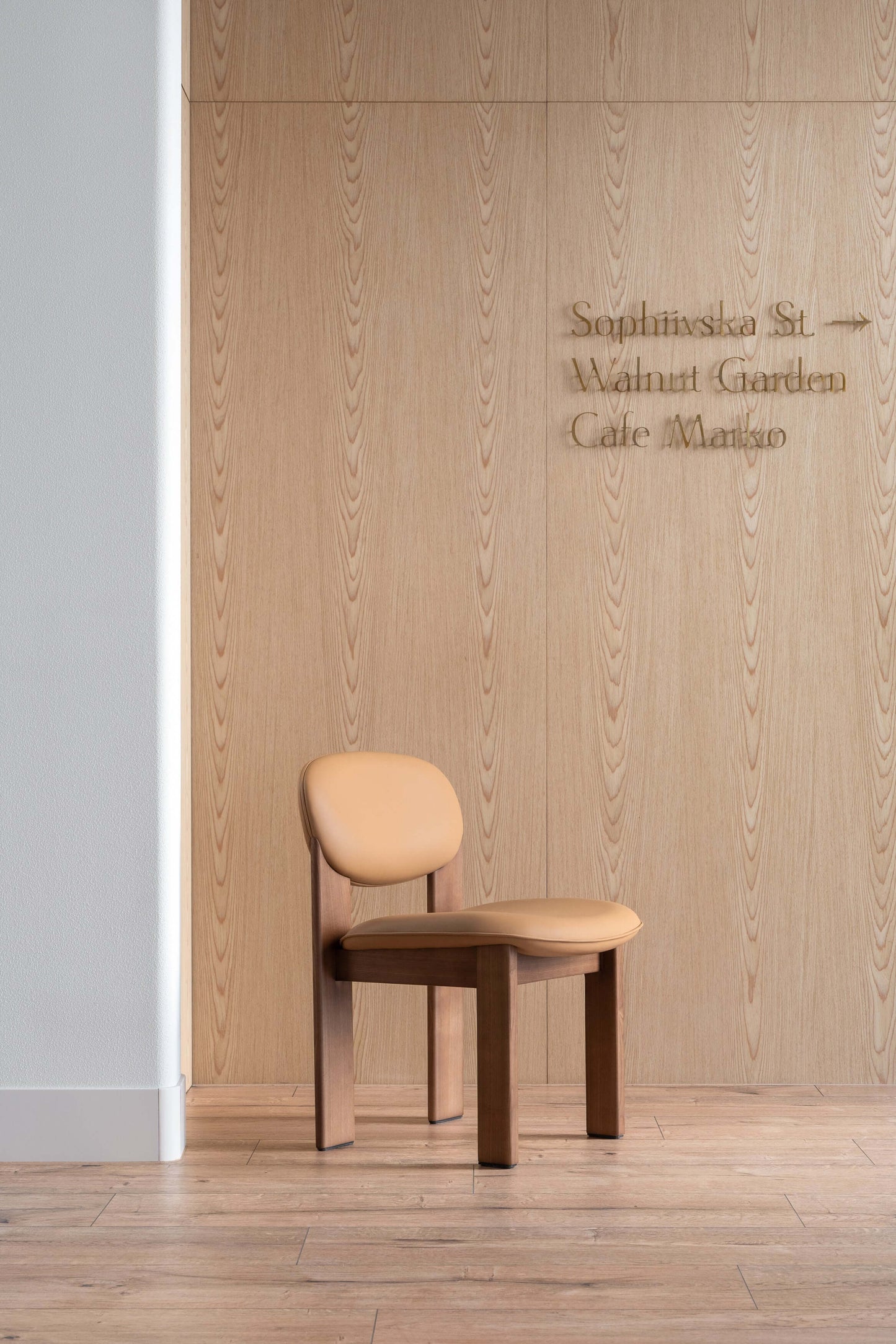 Modern minimalist Archipen chair by Noom, designed by Kateryna Sokolova, with flat twisted legs against a wood panel wall.