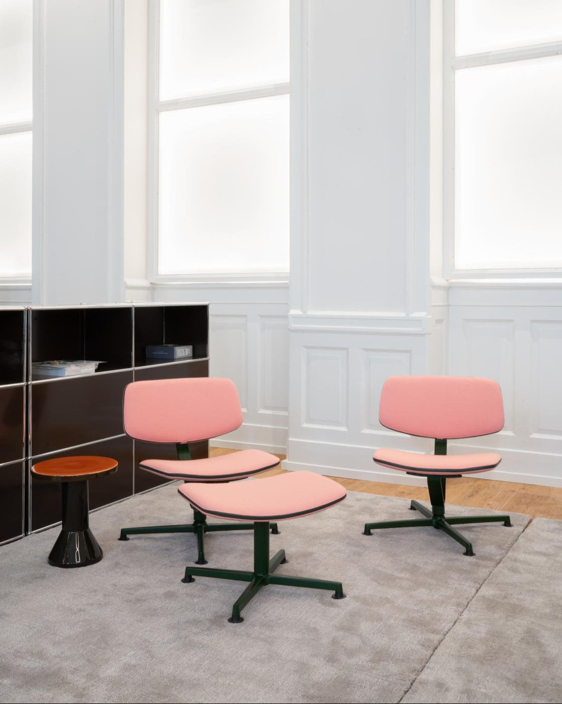 Modern office chairs with pink seats and green bases in a bright room with large windows.