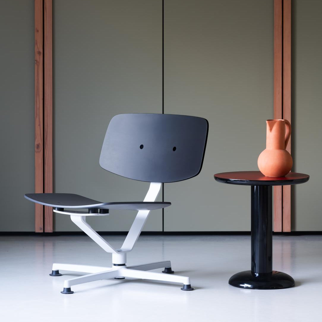 Modern gray chair with white base next to a small round table with an orange vase against a green wall.