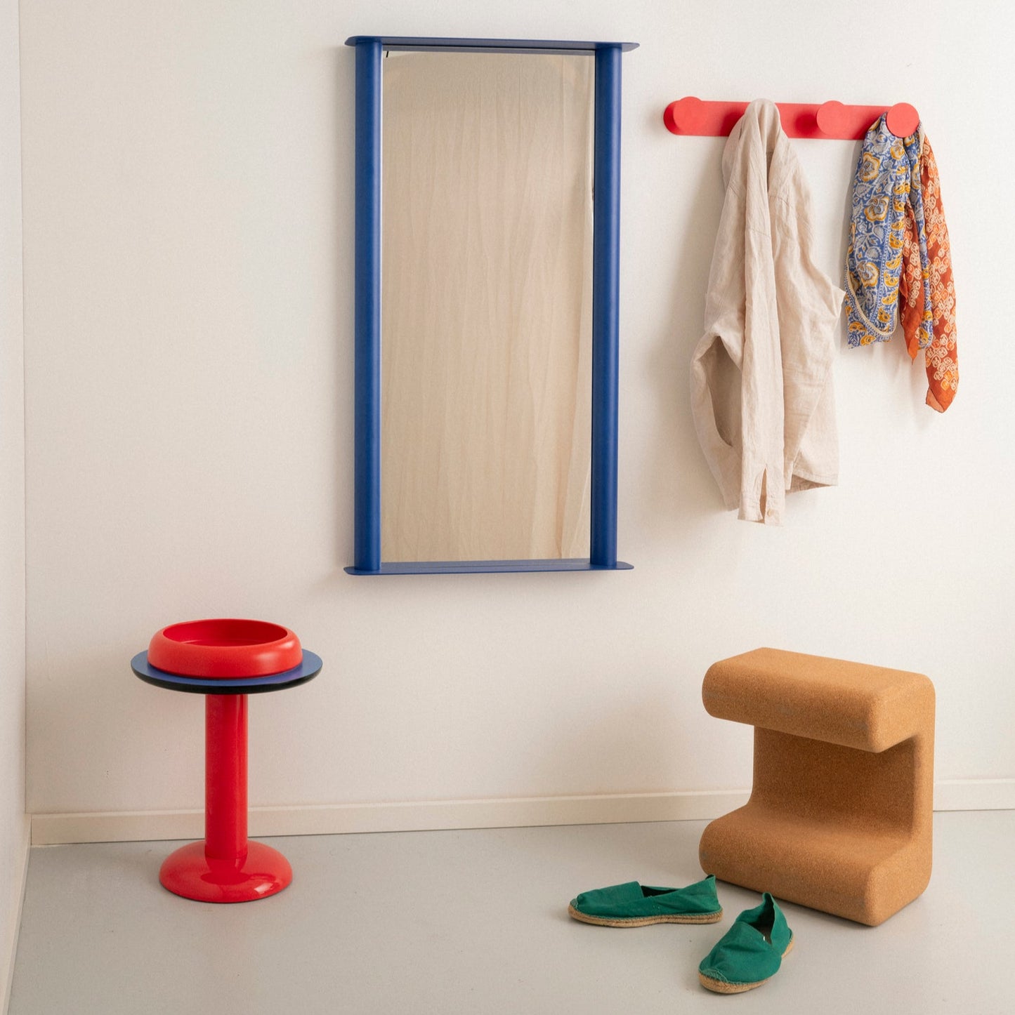 Modern interior with a mirror, coat rack, stool, and shoes on a light gray floor.