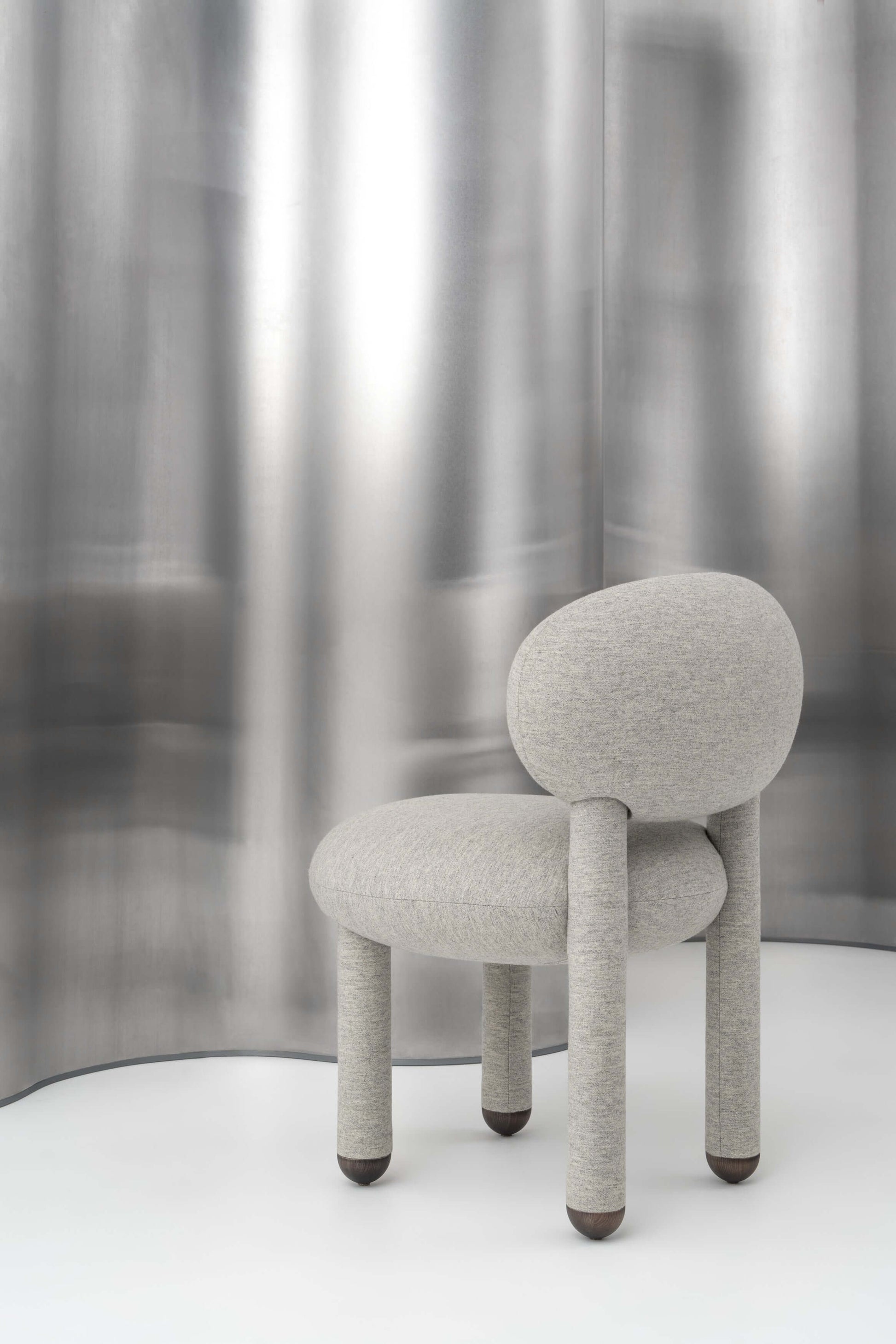 Modern designer flock dining chair by NOOM, featuring soft curves and natural materials against a metallic backdrop.