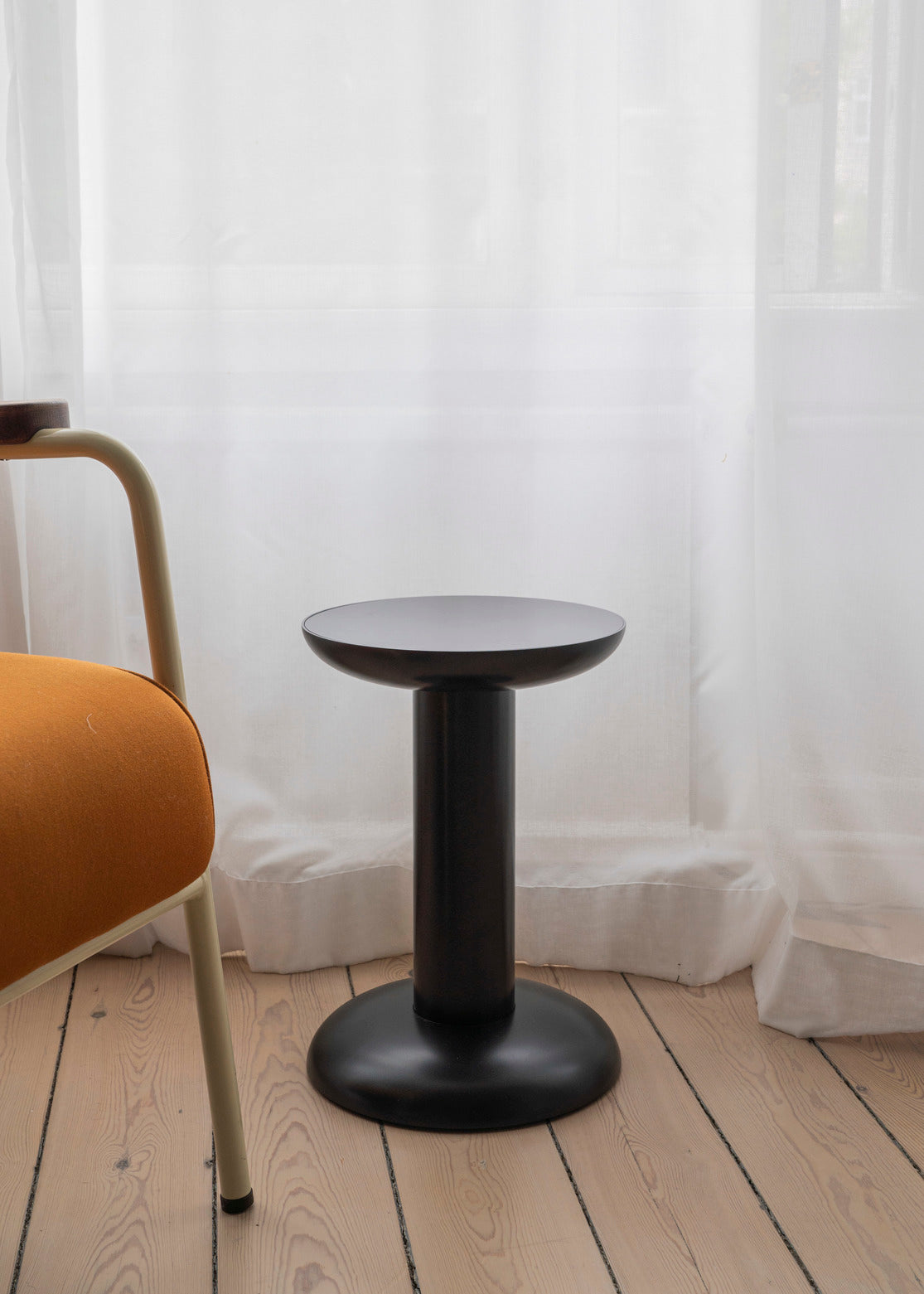 Black stool on a wooden floor with a white curtain background