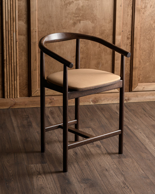 Wooden bar stool with beige cushion against a wooden paneled wall.