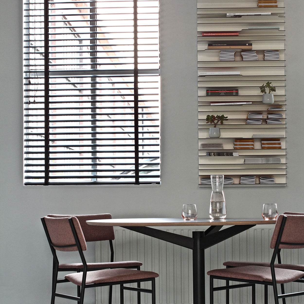 Spectrum Paperback shelving system displayed on wall with modern table and chairs in a stylish interior.