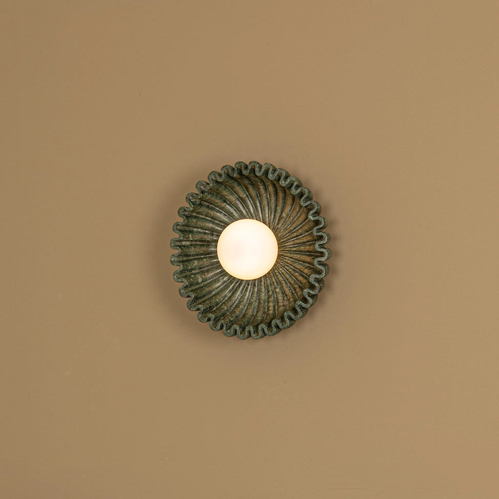 Designer marble circular wall sconce by Simone et Marcel, featuring a unique ruffled design and warm diffused light.