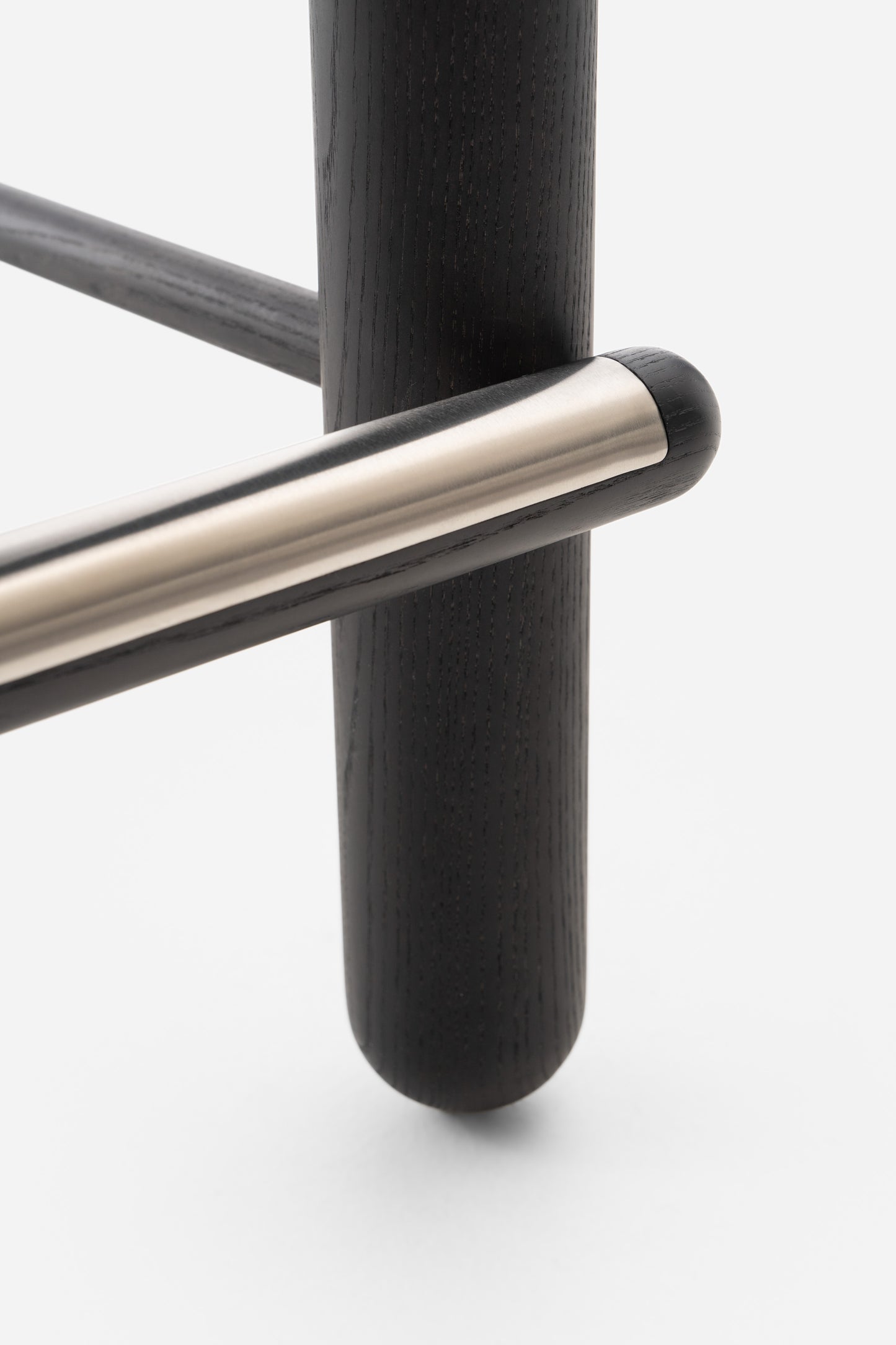 Close-up detail of the Flock CS2 Bar Stool's black wood leg and sleek metallic crossbar design by Noom.