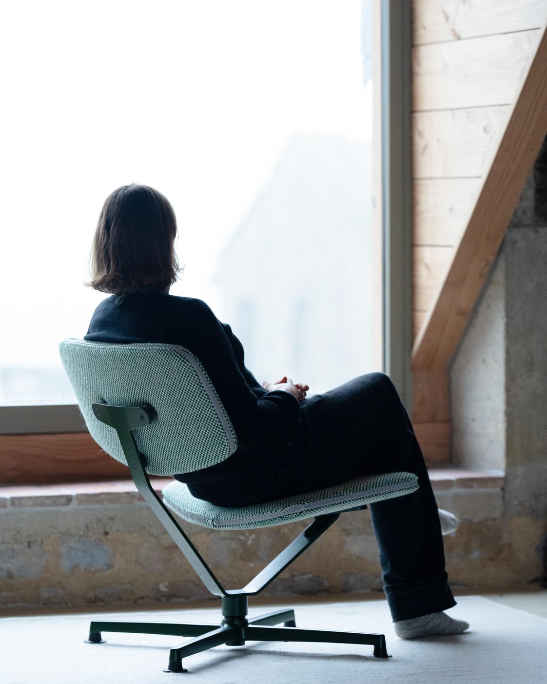 Person sitting on a modern chair by a window in a room with wooden beams.