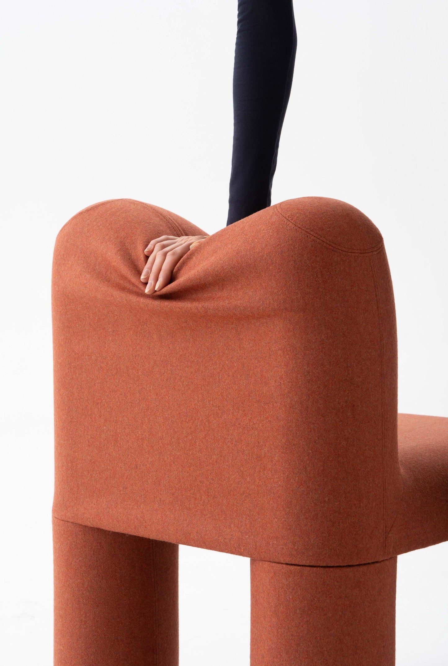 Modern Hello chair by Noom with playful design, featuring a hand pressing on the soft, rounded backrest in a warm orange tone.