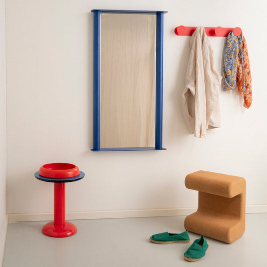 Modern interior with a mirror, coat rack, stool, and shoes on a light gray floor.