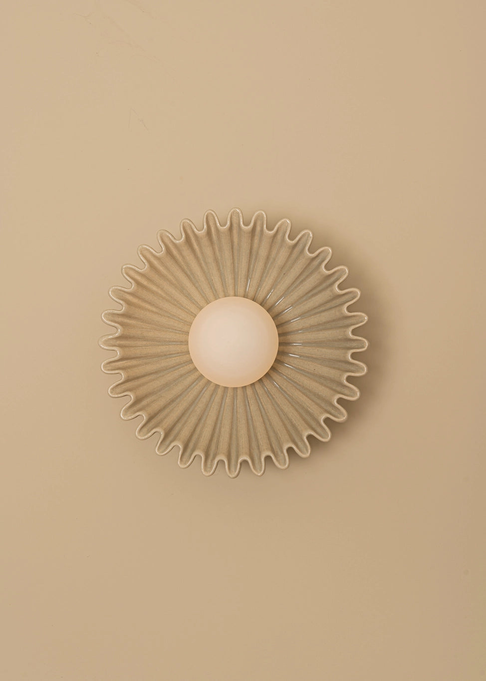 Designer circular wall sconce with radiating edges and central light on a beige wall. Sophisticated and modern lighting accent.