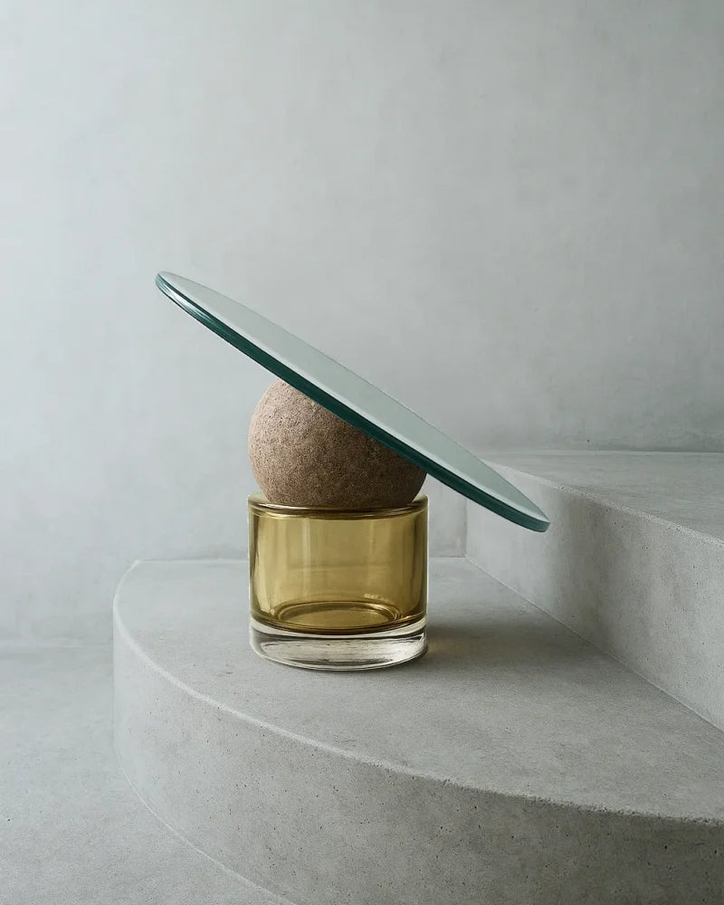Glass vase with a round object on a curved stone surface against a light gray background