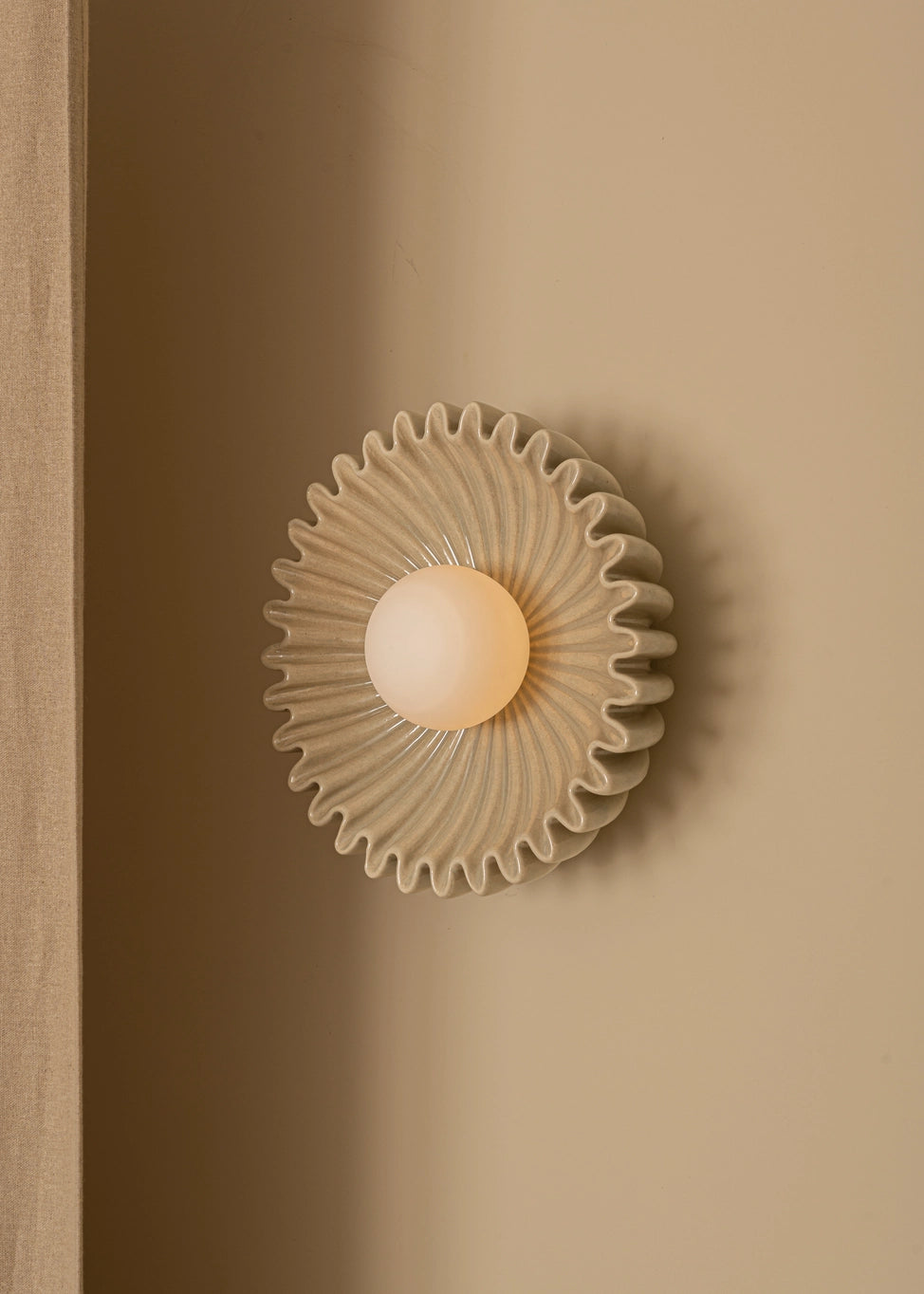 Elegant designer wall sconce with a circular ribbed design and warm glowing light on a neutral wall.