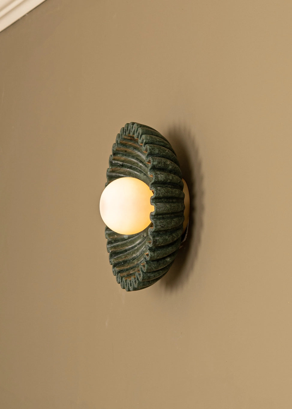 Designer marble circular wall sconce by Simone Et Marcel, featuring green marble and soft, warm light on a beige wall.